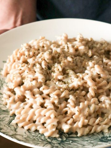 Handen die een bord met pasta vast houden