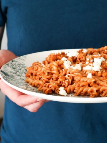 Een close up van pasta met rode pesto en kaas op een bord