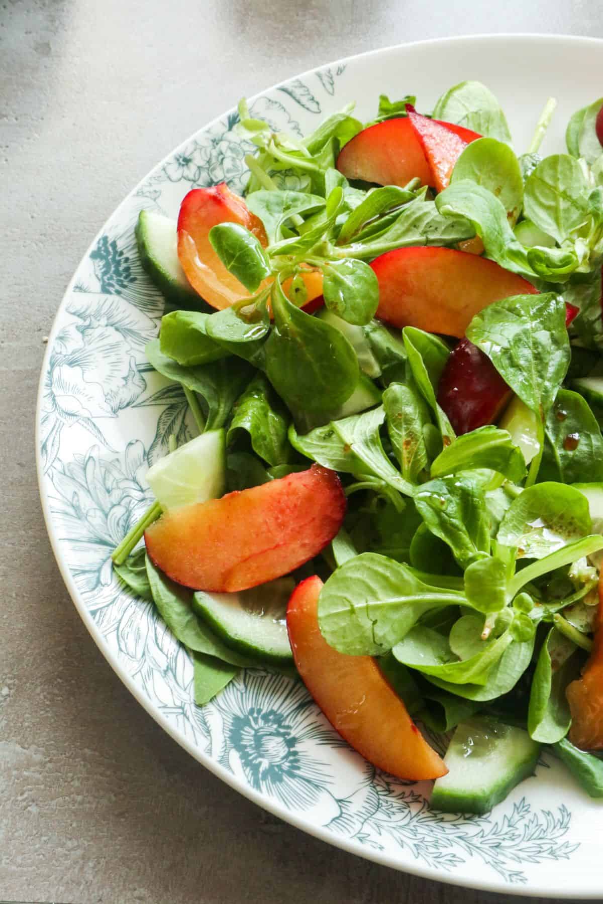 Een pruimen salade met veldsla, spinazie en dressing op een bord