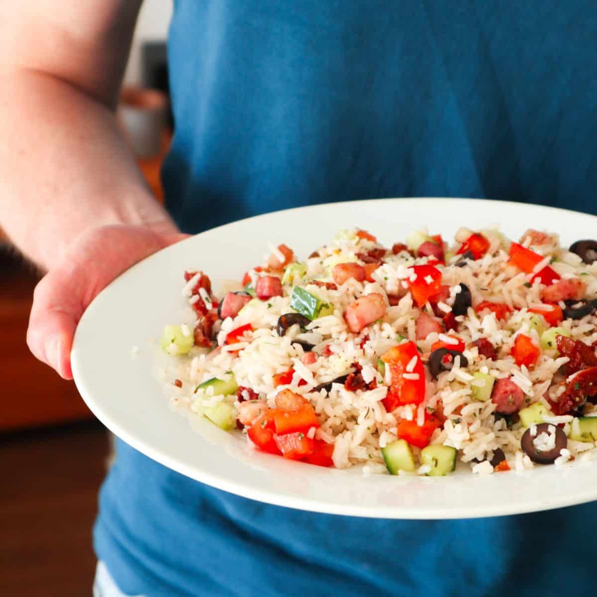 salade van rijst, komkommer, zongedroogde tomaten, paprika en spekjes op een wit bord